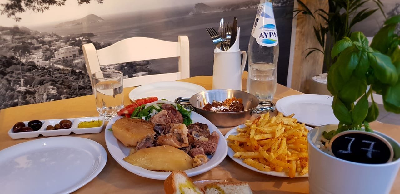 A table set with kleftiko, salad, fries and dips in the garden