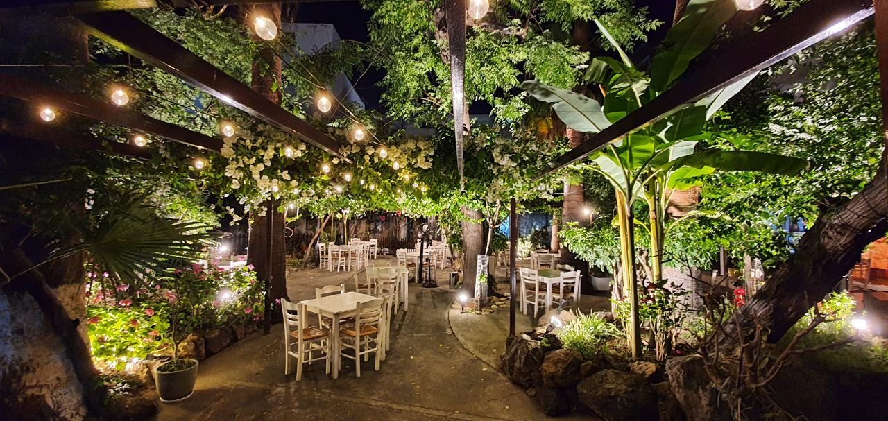 The Ithaki garden at night, tables set beneath string lights and palms